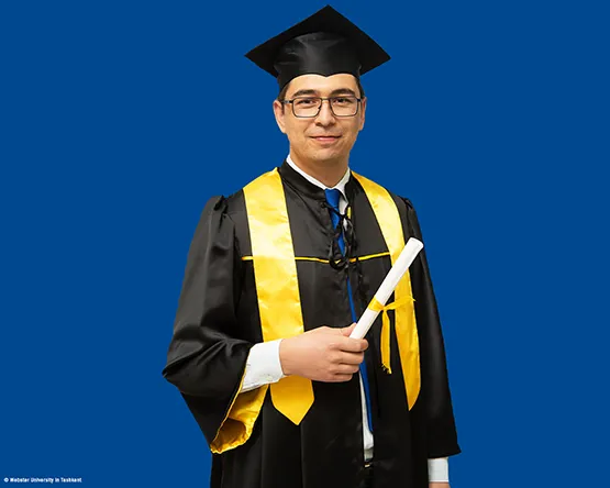 MBA Alumnus Ibrokhimkhon Akhmadkhonov in his commencement gown looks into the camera