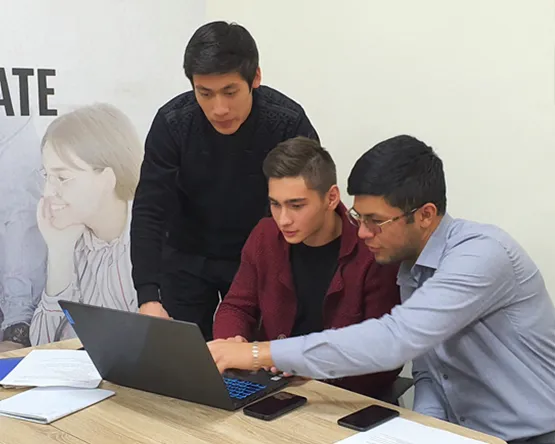 Three male Tashkent students pointing to a laptop screen, while smiling and discussing what they see