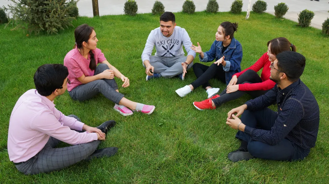 Professor talking to students sitting on grass outside on campus.